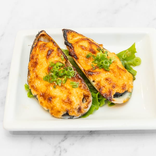 Two baked mussels topped with golden cheese and green onions, served on lettuce on a white plate.