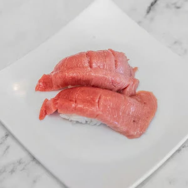 Two pieces of red tuna nigiri sushi with scored fish on a white rectangular plate.