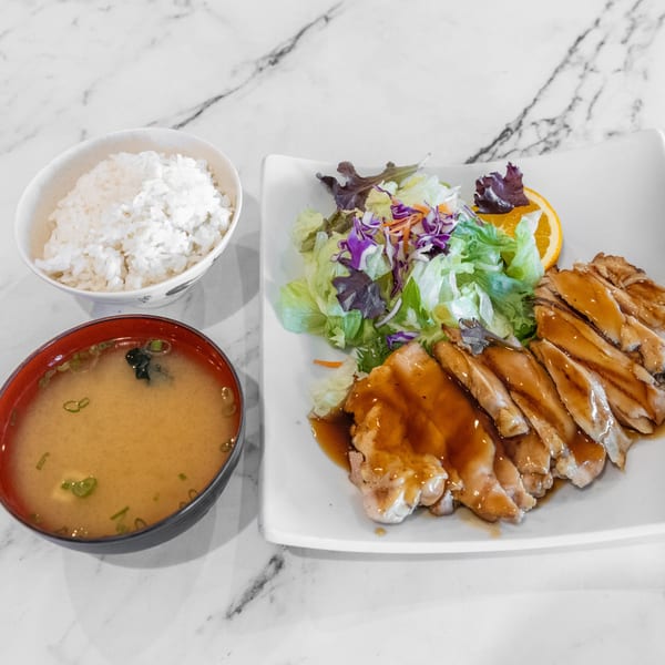 Yashima Restaurant's teriyaki chicken with salad, rice, and miso soup on a marble table.