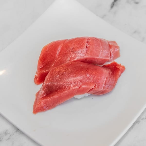 Two pieces of fresh red tuna nigiri sushi on a white rectangular plate.