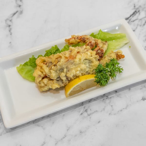 Crispy fried soft-shell crab tempura with lettuce, a lemon wedge, and parsley on a white plate.