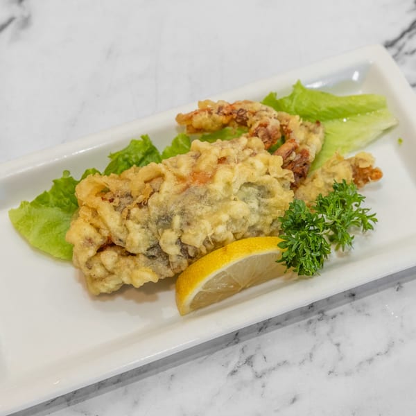 Crispy fried soft-shell crab tempura, garnished with lettuce, parsley, and a lemon wedge on a white plate.