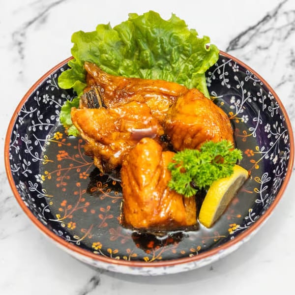 Glazed Japanese chicken pieces with lettuce, parsley, and a lemon wedge in a decorative bowl.
