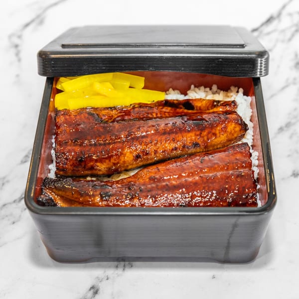 Yashima Restaurant's Unagi Don, grilled eel over rice with yellow pickled daikon in a black bento box.