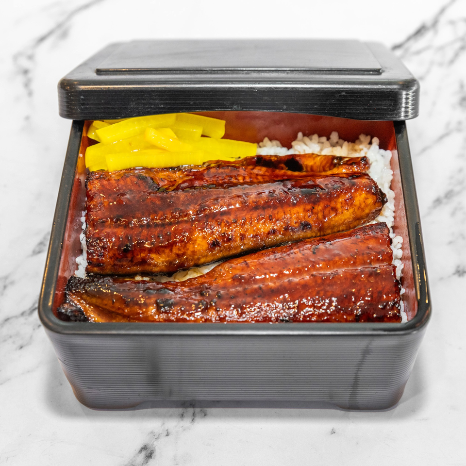 Yashima Restaurant's Unagi Don, grilled eel over rice with yellow pickled daikon in a black bento box.