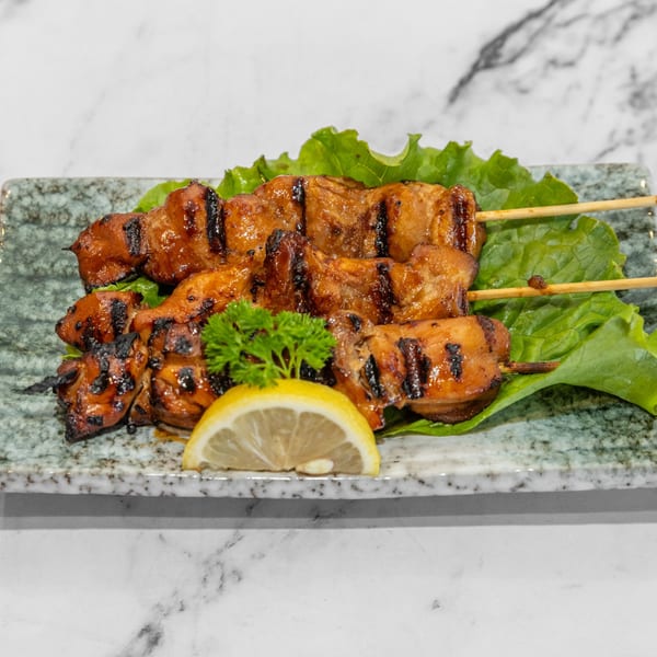 Two skewers of grilled chicken yakitori on lettuce with a lemon slice and parsley.