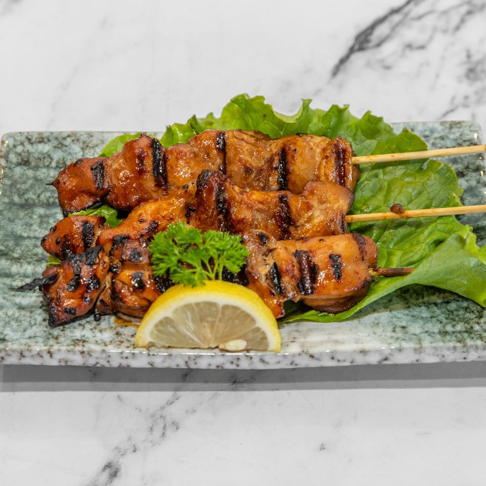 Two skewers of grilled chicken yakitori on lettuce with a lemon slice and parsley.