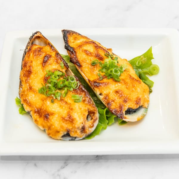 Two baked mussels topped with golden cheese and green onions, served on lettuce.