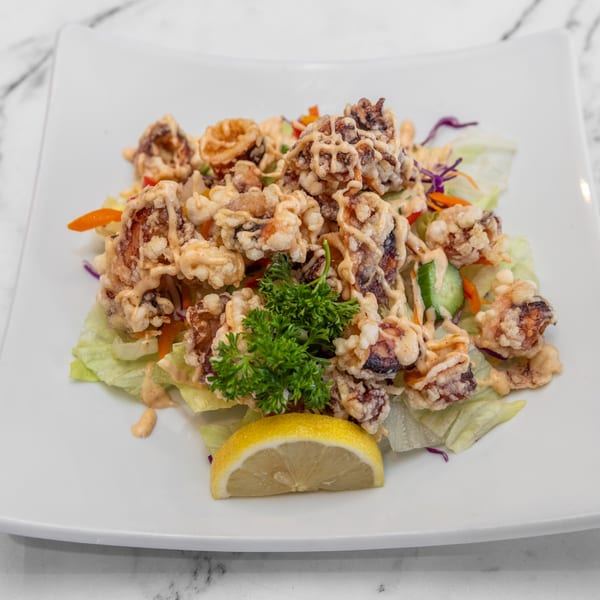 Crispy fried calamari with a creamy sauce, fresh lettuce, and a lemon wedge on a white plate.