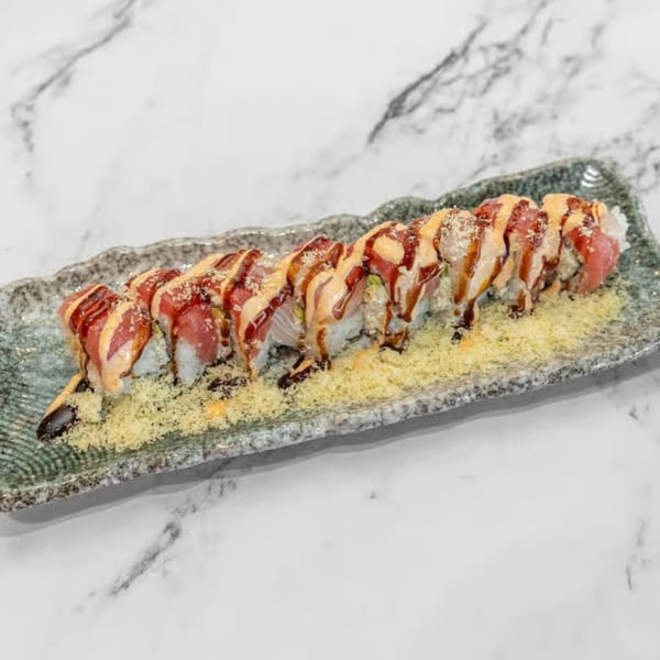 A long sushi roll with tuna, salmon, and sauces on a gray rectangular plate.