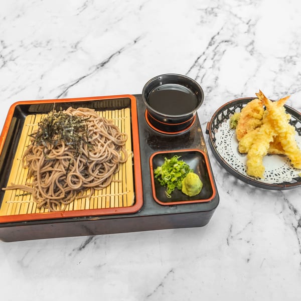 Japanese soba noodles with nori, dipping sauce, wasabi, scallions, and tempura shrimp on marble.