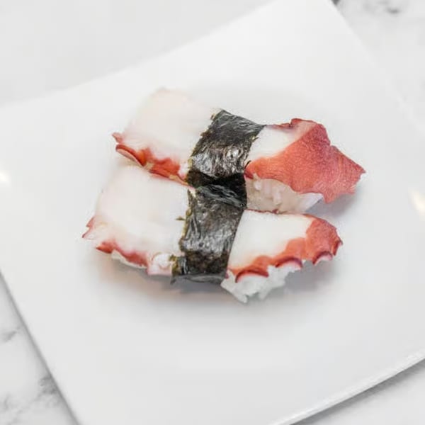Two pieces of octopus nigiri sushi, with white rice and pinkish-white octopus, on a white plate.
