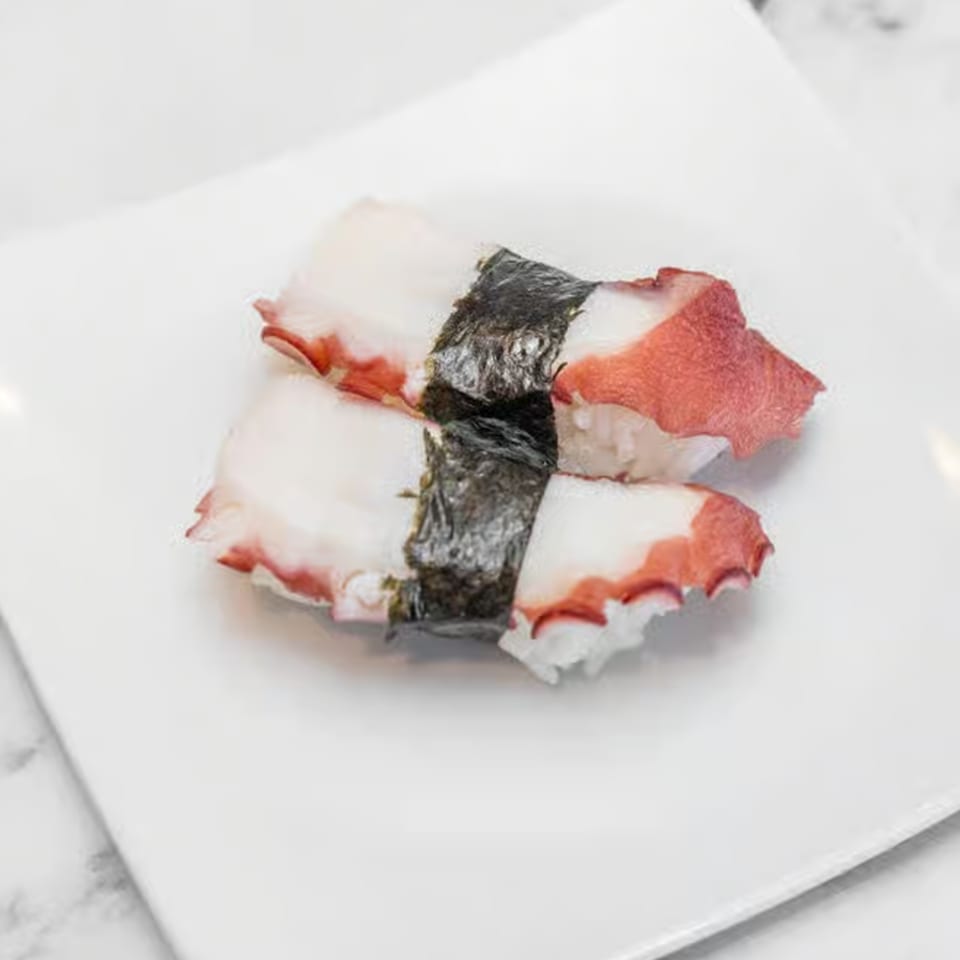 Two pieces of octopus nigiri sushi, with white rice and pinkish-white octopus, on a white plate.