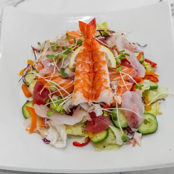A vibrant Japanese sashimi salad with shrimp, various fish, fresh greens, and lemon on a white plate.
